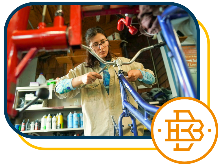 Woman in Bike Barn tightening bolt on blue bicycle frame, wearing safety glasses