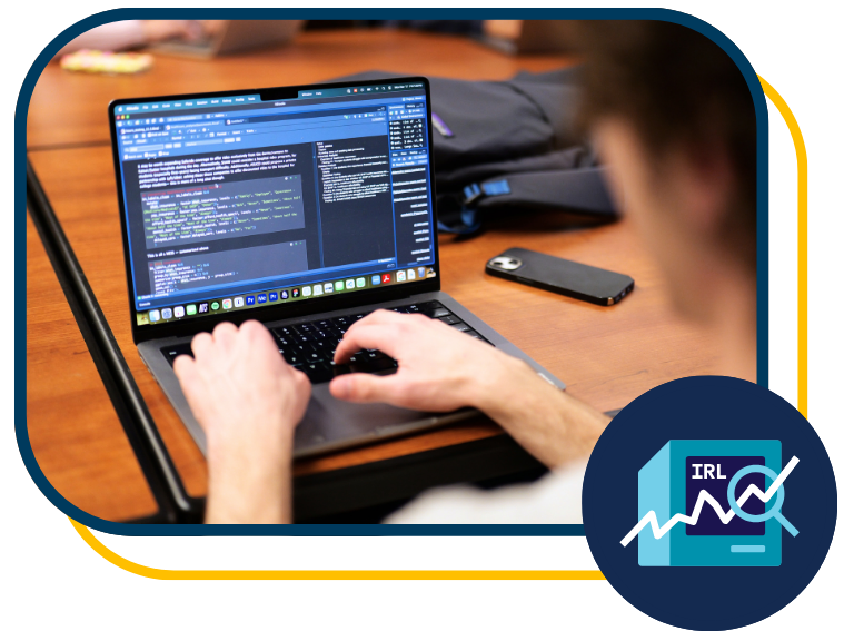 Person typing code on laptop at wooden desk, phone and glasses nearby